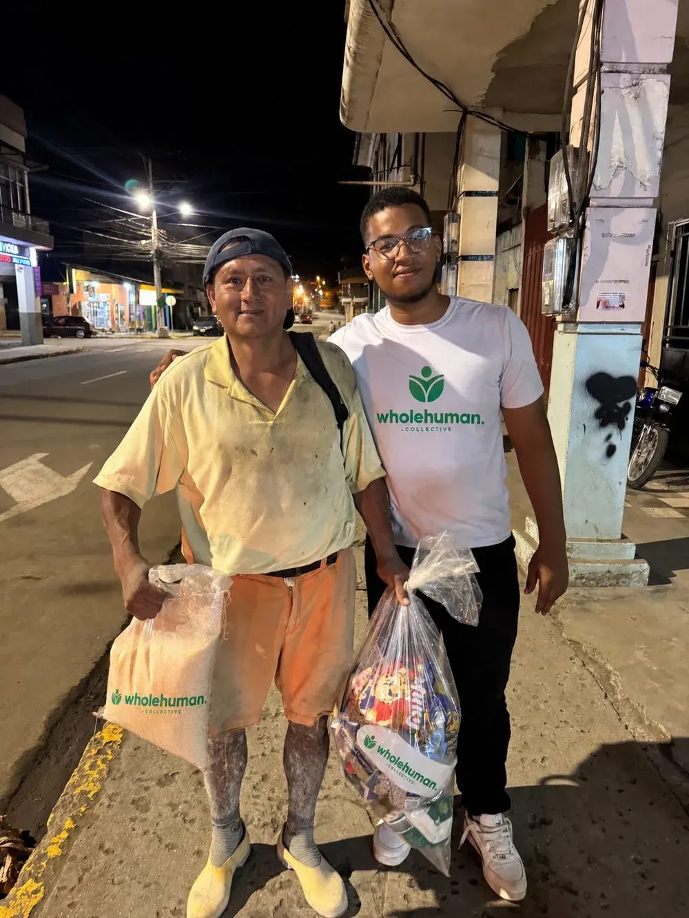 A man holding groceries beside a Wholehuman team member on a street at night