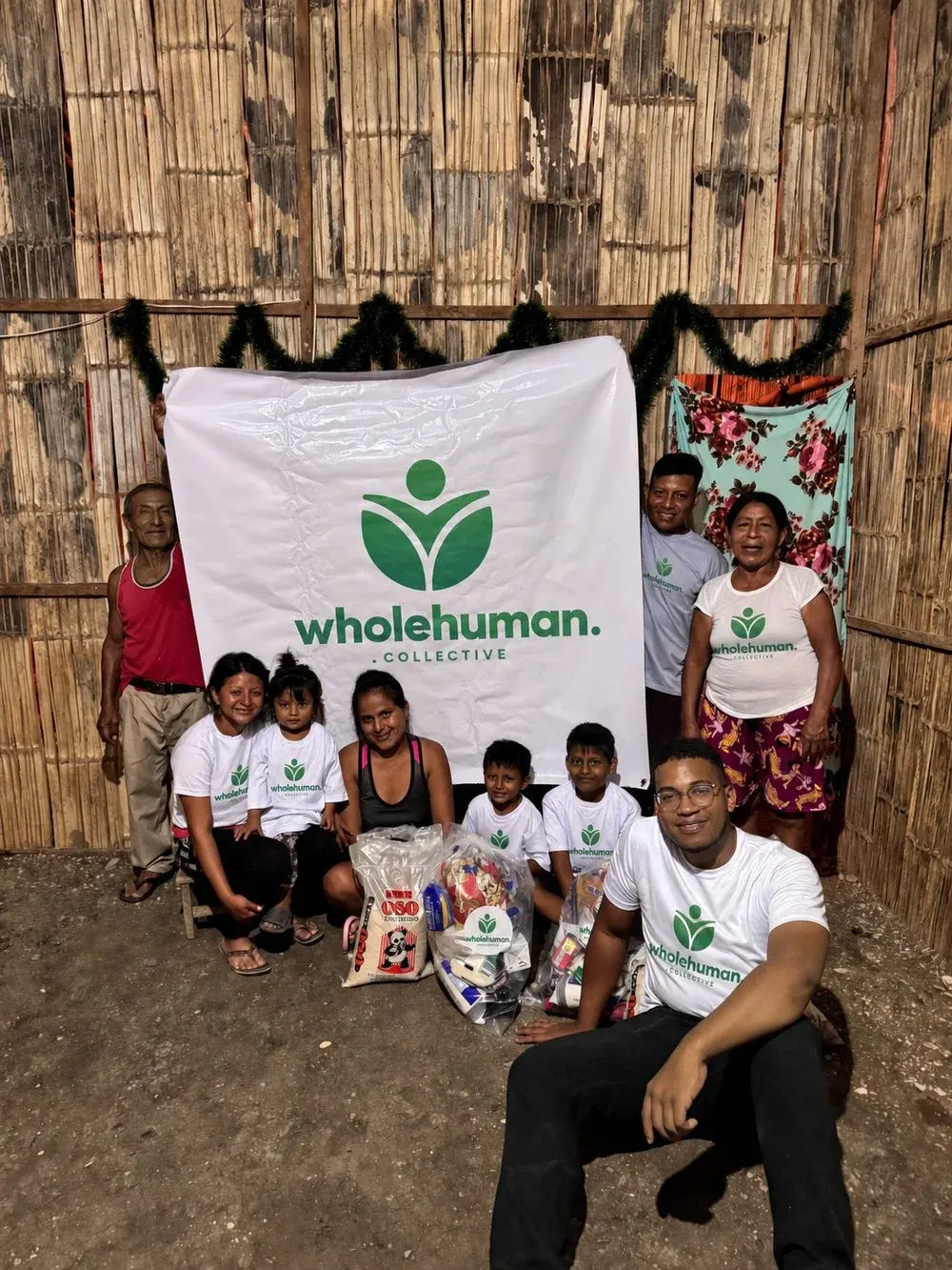 Three generations of a family with Wholehuman team members in front of a Wholehuman Collective banner, bags of food at their feet
