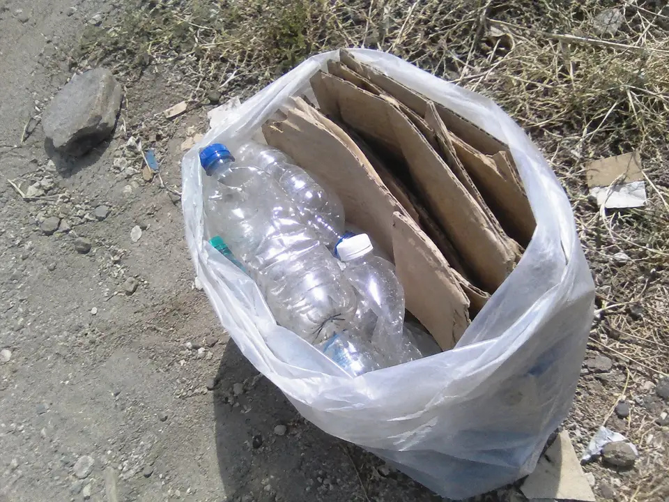 Illustrative image of bottles and cardboard in a bag on a dirt roadside